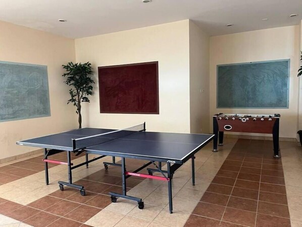 A room with a ping pong table, a foosball table, and a large red painting on the wall.