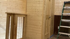 Een kamer met houten wanden en een deur, een ladder, en diverse gereedschappen en bouwmaterialen op de vloer.