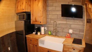 Een kleine keuken met houten kastjes, een inbouwmagnetron, een roestvrijstalen koelkast, een spoelbak en een flatscreen televisie aan de muur.