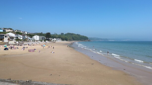 A wide sandy beach with buildings and trees in the background.