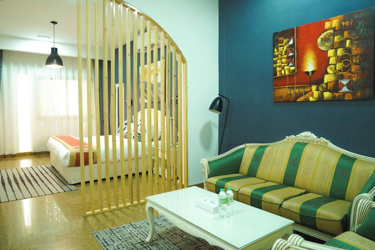 A living room with a green and yellow sofa, a white coffee table, a wooden partition, and a painting on the wall.