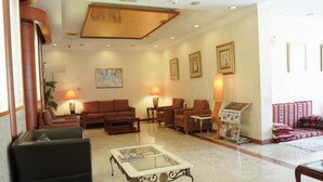 A spacious lobby with leather sofas, a coffee table, and a reception area with a magazine rack. - Safeer International Hotel (Muscat)