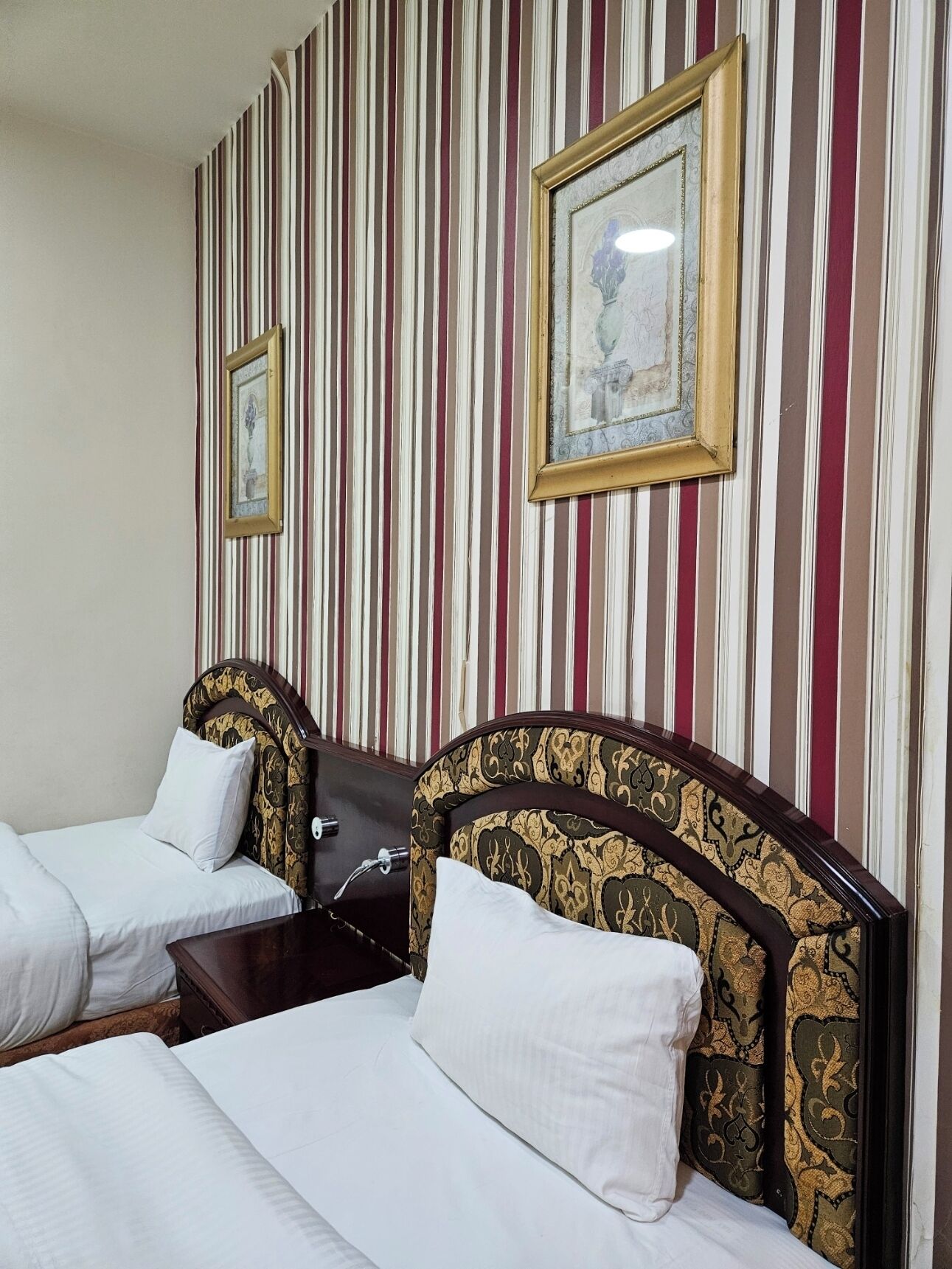 A hotel room with two single beds, striped wallpaper, and framed artwork on the wall.