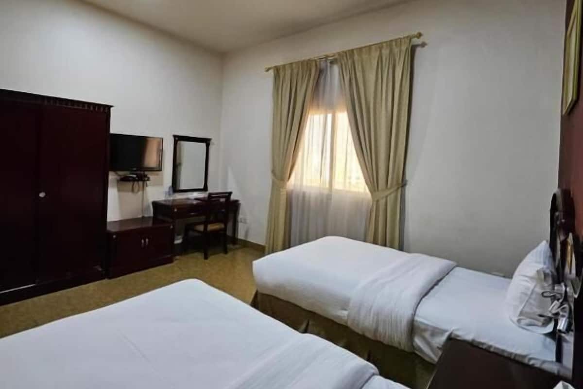 A hotel room with two single beds, a desk, a chair, a wardrobe, and a television.