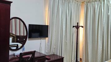 A hotel room with a bed, a desk with a chair, a television, a mirror, and a floor lamp.