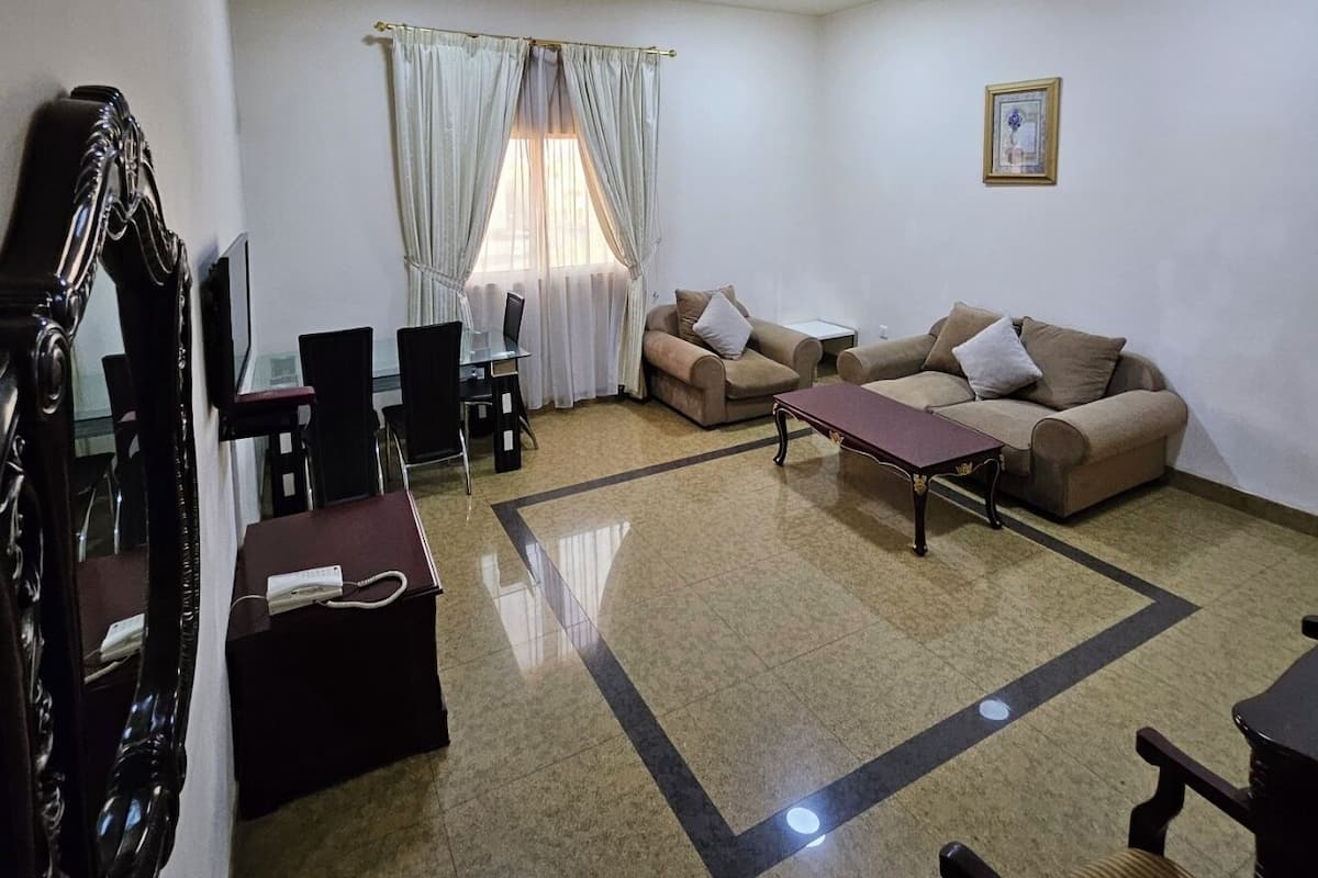 A living room with a sofa set, a dining table with chairs, a TV mounted on the wall, and a large mirror.
