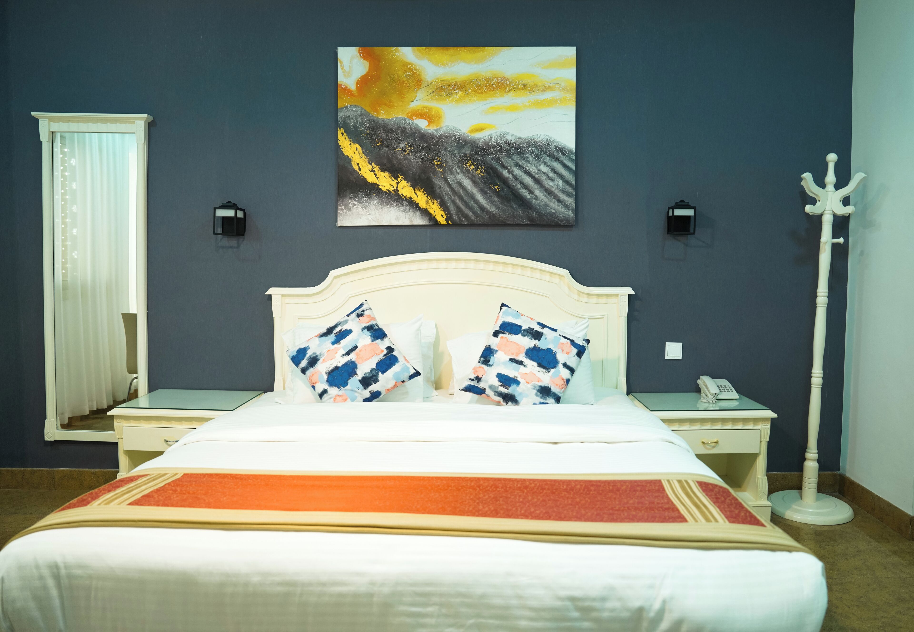 Een hotelkamer met een bed, een nachtkastje met een telefoon, een wandlamp en een schilderij boven het bed.