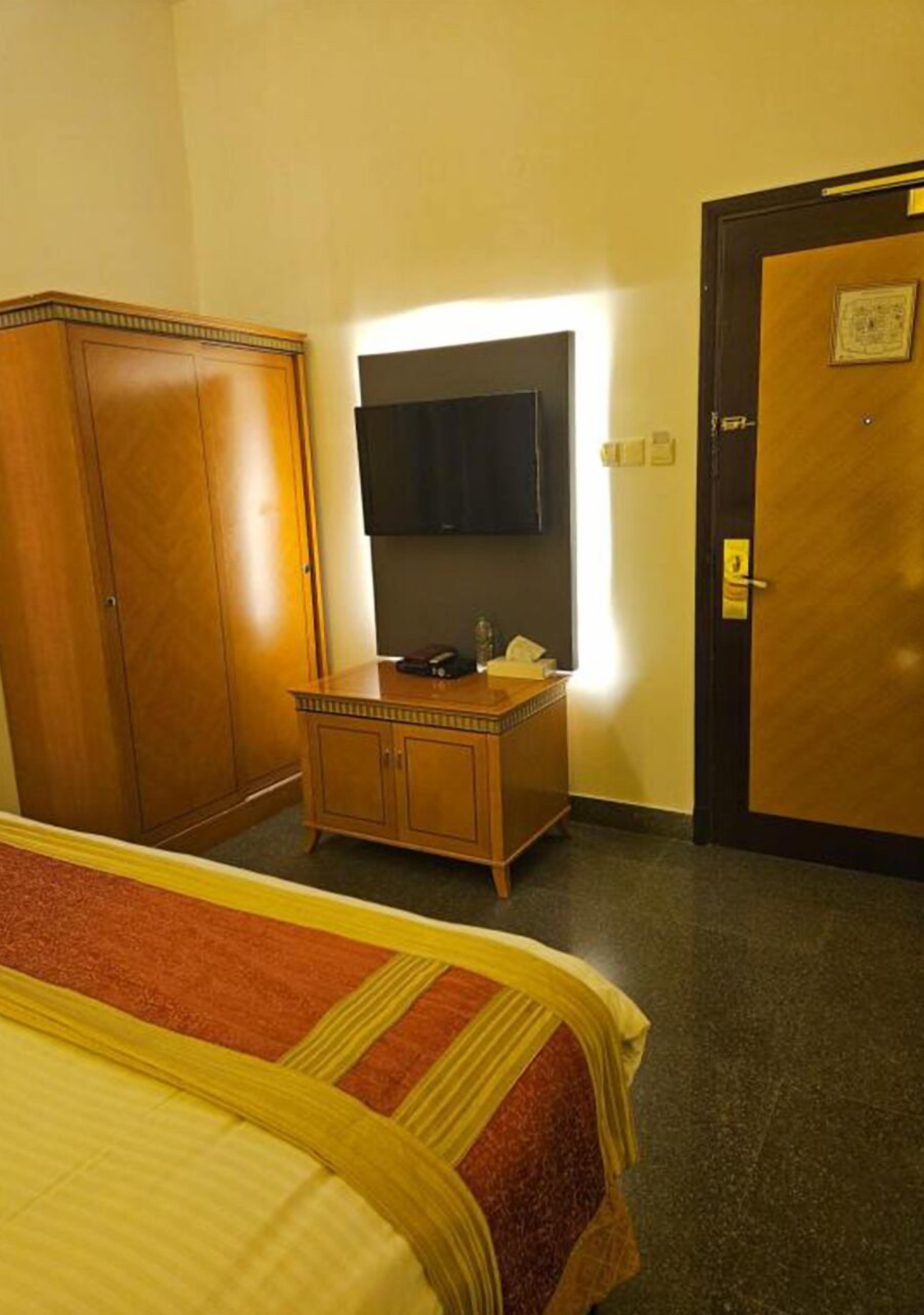 A hotel room with a bed, a wooden dresser, a mirror, and a door.