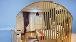 A compact room with a curved ceiling, a bed, a desk, a chair, a small table, and a hanging light fixture. - Safeer International Hotel (Muscat)