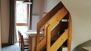 A kitchen with wooden stairs, a dining area with chairs, and a window with curtains.