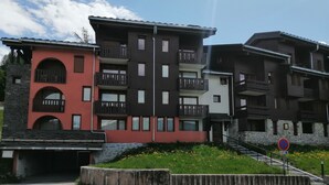 A multi-story building with balconies, a stone facade, and a parking area.