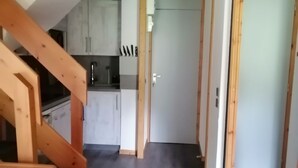 A narrow hallway with a wooden staircase on the left, leading to a kitchen area with white cabinets and a black countertop.