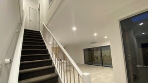 A modern staircase with a handrail, leading to a room with a large sliding glass door and a ceiling-mounted air conditioning unit. - Unfurnished-2 Story 3 Bedroom House- 30min to Melbourne international Airport (South Morang)