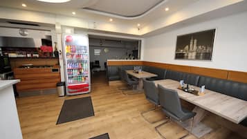 Un restaurant avec un plancher en bois, un distributeur de boissons gazeuses et un espace où l’on peut s’asseoir, avec des tables et des chaises.