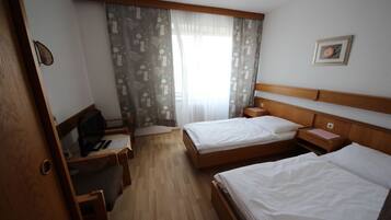 Et hotelværelse med to senge, et skrivebord med stol, et fjernsyn og et vindue med gardiner.