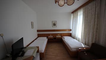 Habitación de hotel con dos camas individuales, un escritorio con computadora, una silla y un sofá.