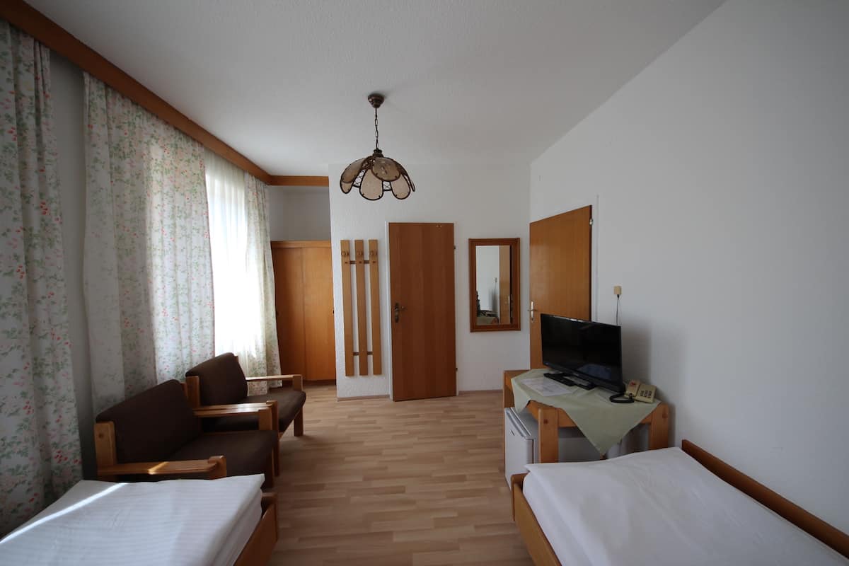 A hotel room with two single beds, a sofa, a television, and a desk with a telephone.