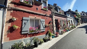Une rangée de maisons en briques rouges, avec des volets blancs aux fenêtres, des plantes en pot et un ciel d’un bleu éclatant.