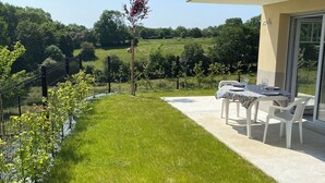 Une terrasse avec une table et des chaises, un jardin clôturé et une vue sur un paysage verdoyant.