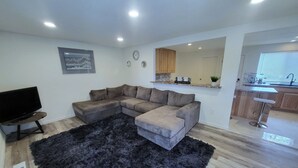 A modern living room with a sectional sofa, a flat-screen TV, and a black furry rug. - Linda Casa peaceful neighborhood  (Aurora)