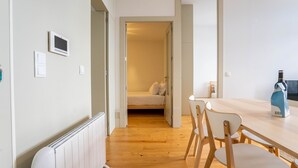 Una habitación moderna y minimalista con suelo de madera, una cama con ropa blanca, una mesa de comedor de madera con sillas y una botella de vino sobre la mesa.
