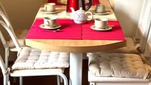 Ein Esstisch mit roter Tischdecke, weißen gepolsterten Stühlen und einer weißen Teekanne.