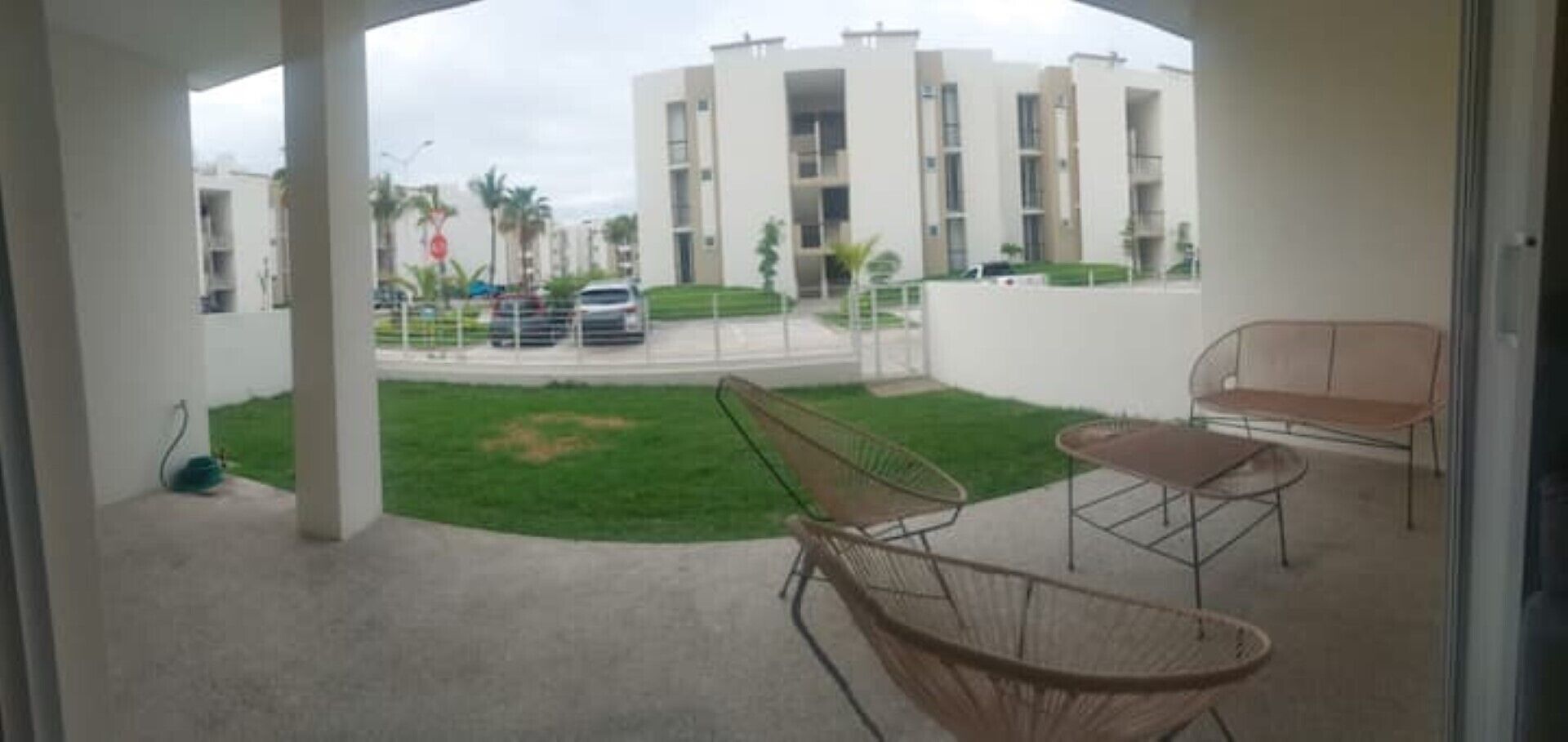 Un balcone con vista su un edificio, una zona verde e un'auto parcheggiata.