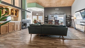 Una sala de estar moderna con un amplio sofá modular, piso de madera y vistas a las montañas a través de las ventanas.