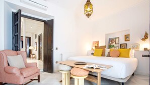 Een moderne slaapkamer met een bed, een houten tafel, een roze fauteuil en een klein krukje.