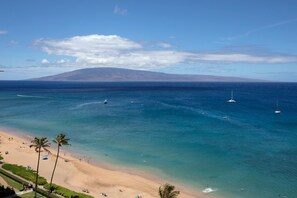 Une plage avec une eau d’un bleu limpide, des palmiers et une montagne en arrière-plan.