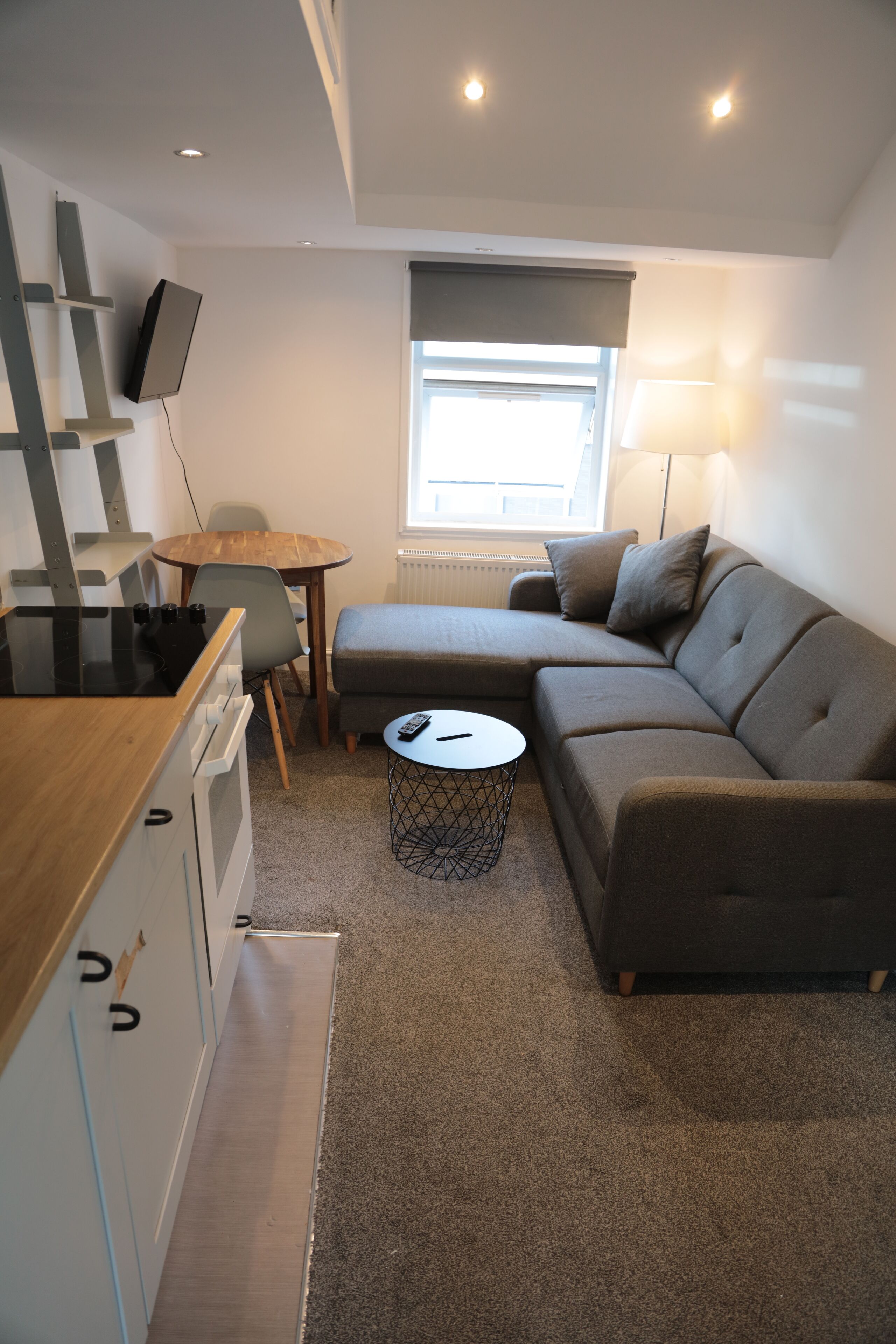 Ein kompakter Wohnbereich mit Küchenzeile, einer Couch, einem kleinen Tisch und einem an der Wand befestigten Fernseher.