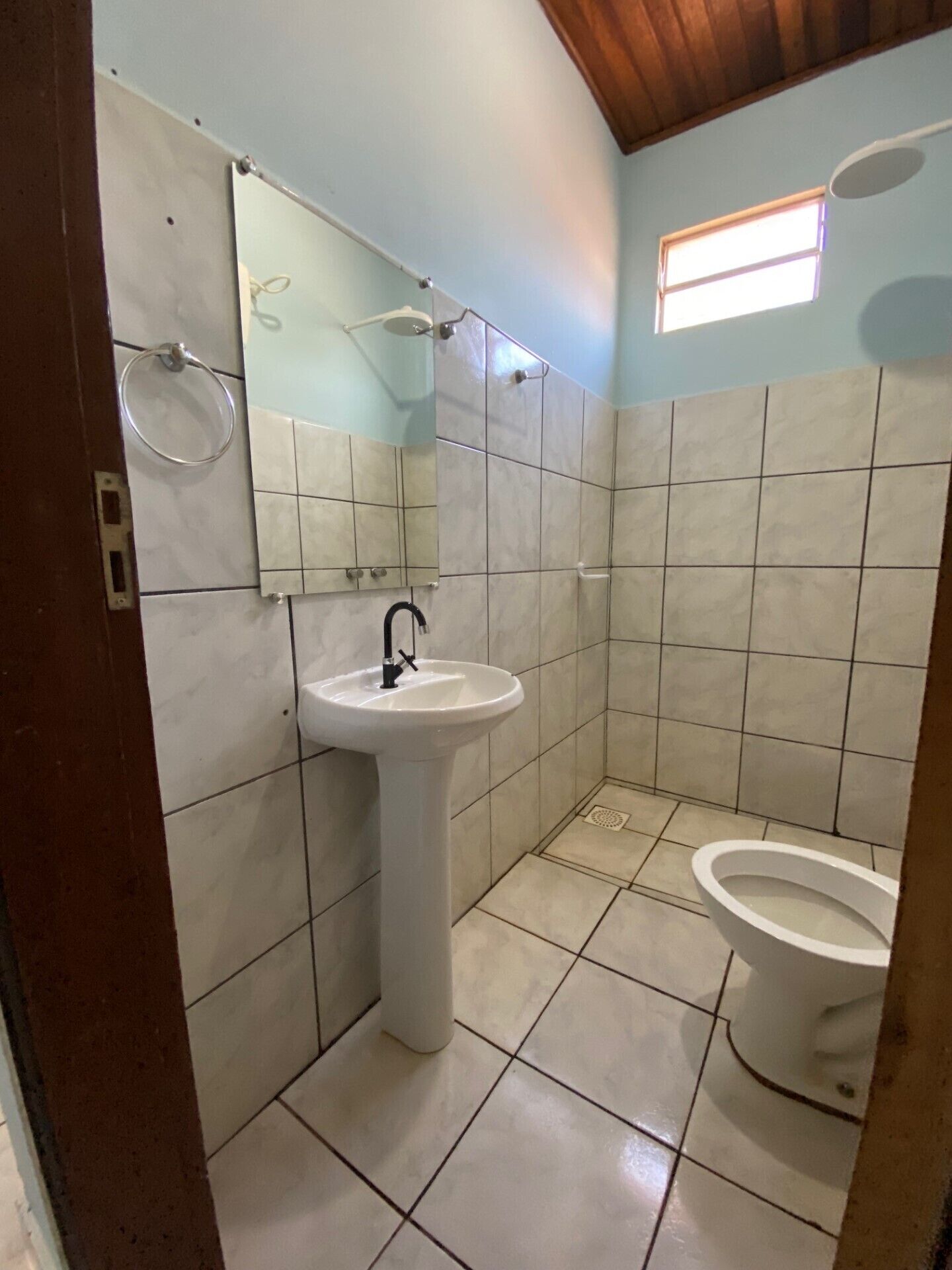A small bathroom with a pedestal sink, a toilet, and a mirror.