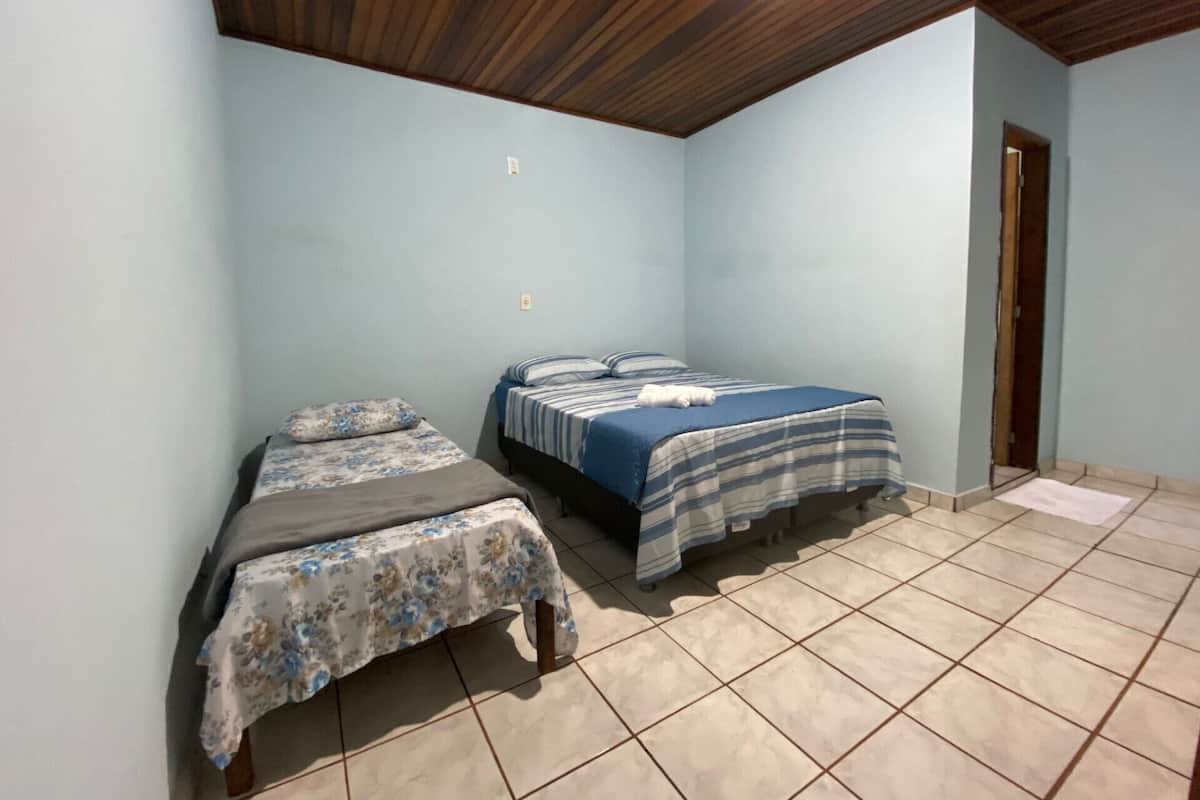 A room with two beds, a wooden ceiling, and tiled flooring.