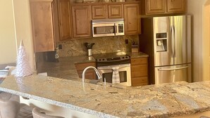 A kitchen with wooden cabinets, stainless steel appliances, a granite countertop, and bar stools. - Sante Fe Style pool home (Lake Havasu City)