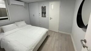 Un dormitorio con cama, una puerta, aire acondicionado instalado en la pared y un espejo.