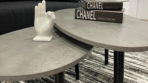 Una sala de estar moderna con una mesa redonda gris, una escultura de mano blanca y dos libros titulados 'CHANEL COMPACT NATURE'.