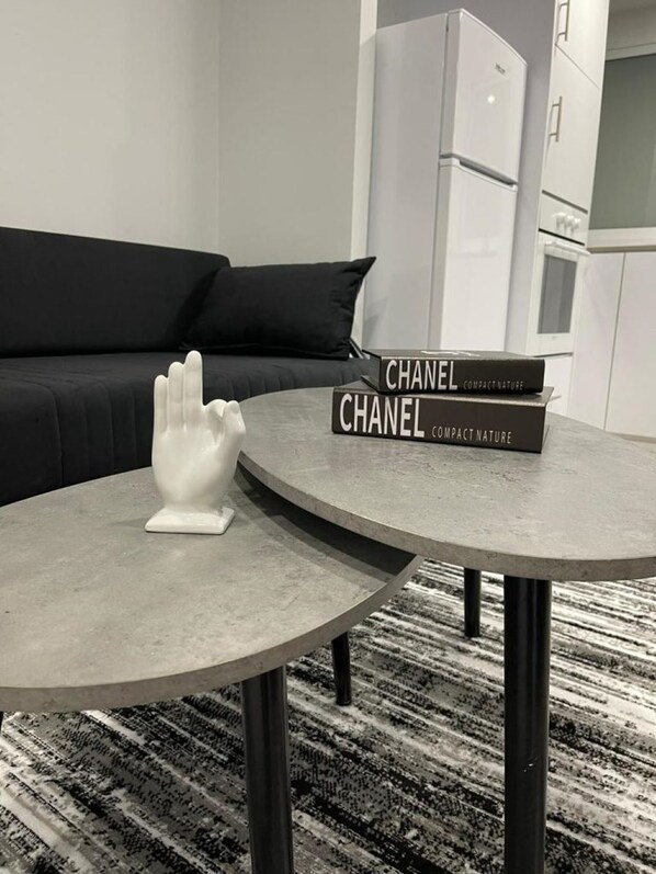A modern living room with a round grey table, a white hand sculpture, and two books titled 'CHANEL COMPACT NATURE'.