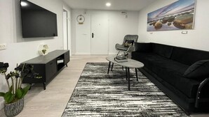 Una sala de estar moderna con un sofá negro, un mueble de entretenimiento negro, un televisor de pantalla plana, una mesa de centro redonda y una alfombra con estampado blanco y negro.
