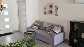 Una sala de estar con un sofá gris, una mesita redonda y un mueble negro con adornos.