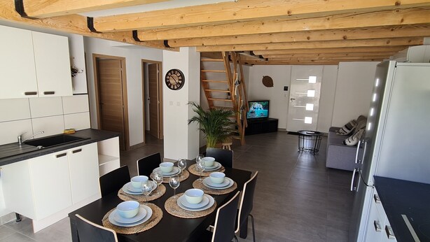 Una cocina moderna con armarios blancos, encimera negra y comedor con mesa dispuesta para cuatro.