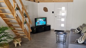 Una sala de estar moderna con una escalera de madera, un televisor sobre un soporte negro, un sofá gris y una pequeña mesa redonda.