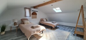 Un dormitorio con dos camas, un tragaluz, un equipo de aire acondicionado y una escalera de madera.