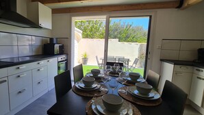 Una cocina moderna con armarios blancos, encimera negra y una zona de comedor preparada para seis personas, con platos, cuencos y vasos.