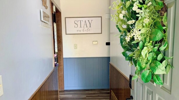 Un passadís amb sòl de fusta, una làmpada al sostre i un cartell fixat a la paret que diu 'STAY at home', i un arranjament decoratiu de plantes a la paret dreta.
