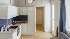 Una cocina moderna con armarios blancos, una isla central y un salpicadero azul. En la sala de estar hay un sofá gris y una mesa de centro blanca.