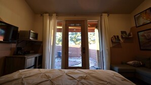A bedroom with a bed, a TV on a stand, a door leading to a balcony, and a couch.