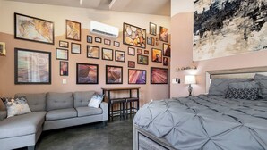 A bedroom with a gray bed, a gray sofa, and a small table. The walls are decorated with various framed artworks. - River Rock Studio w/private courtyard, 20 minutes to Zion (Virgin)