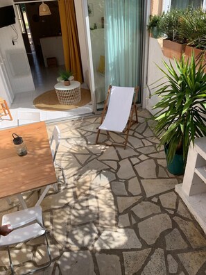 A patio with a stone floor, a wooden table, a white folding chair, and a small round table with a woven basket.