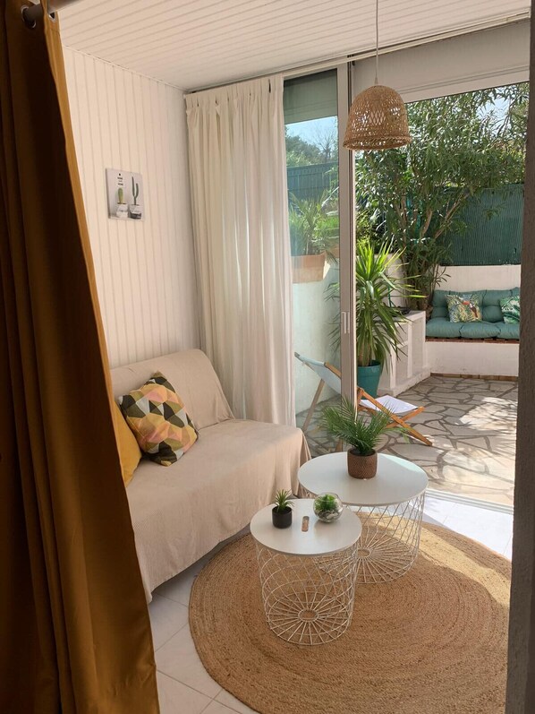 A cozy living area with a sofa, a round table with two chairs, and a large window overlooking a garden.
