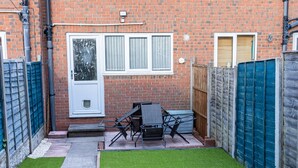 A brick house with a front door, two windows, a small patio with artificial grass, and a blue fence. - Cosy 2bedroom House-perfect for Long & Short Stay (Wolverhampton)